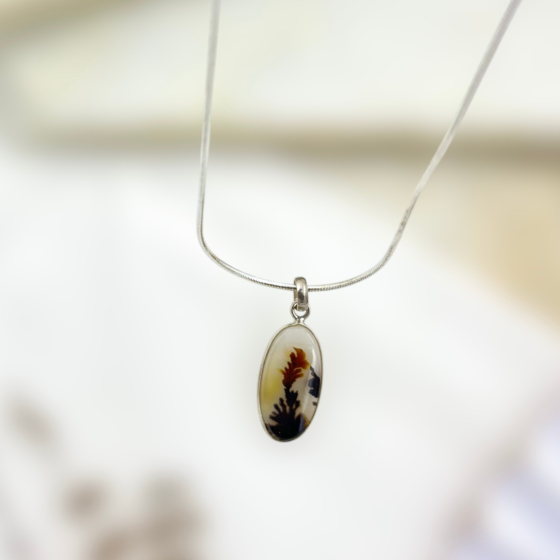 Close-up of the Shazar gemstone showcasing vivid red and black dendritic formations against a soft amber-white background, set in fine silver.