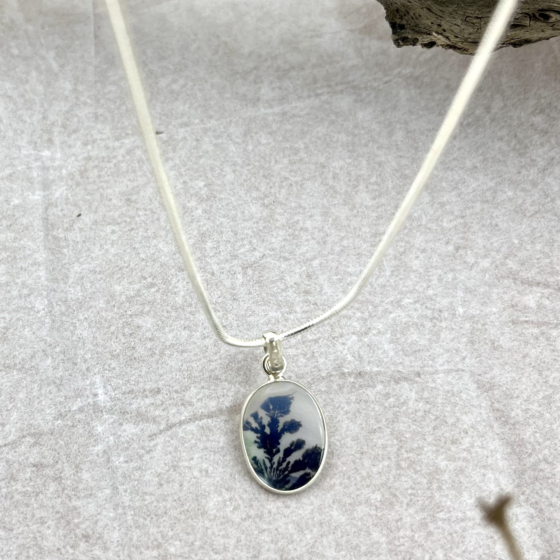 Close-up of the stone’s dark blue dendritic branches rising through a cloudy white matrix—evoking twilight trees in moonlight.