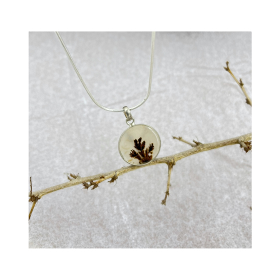Close-up of the gemstone highlighting deep organic dendritic formations fanning out like a fern against a warm beige background.