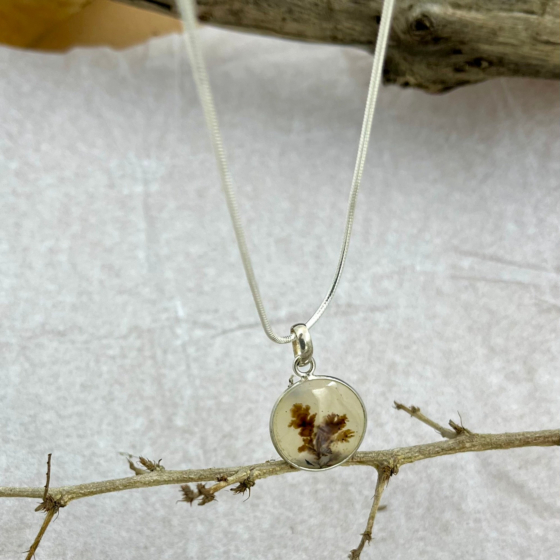Close view of the natural patterns inside the stone, resembling tree branches touched by amber sunset light across a translucent cream background.