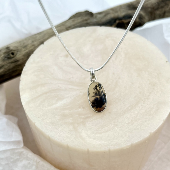 Close-up of Whispered Silhouettes Shazar silver pendant displayed on a beige textured pedestal, highlighting the intricate dark patterns within the gemstone.