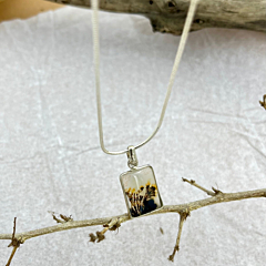 Rectangular Shazar silver pendant titled Forest Dream laid on a soft textured backdrop with rustic wood accents and a delicate silver chain.